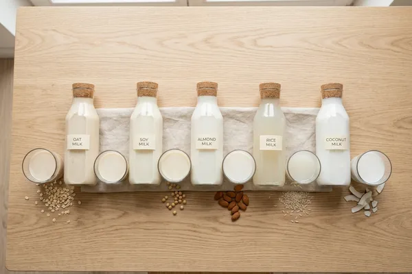 Fünf Gläser mit verschiedenen Pflanzenmilch-Sorten nebeneinander auf einem hellen Tisch