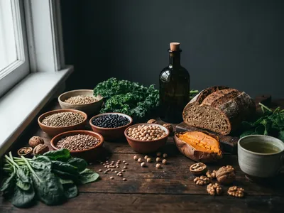 Pflanzliche Langlebigkeits-Lebensmittel in moodiger Stillleben-Anordnung — Linsen, Bohnen, Vollkornbrot, Olivenöl, Süßkartoffel, Blattgemüse, Walnüsse und grüner Tee auf dunklem Untergrund