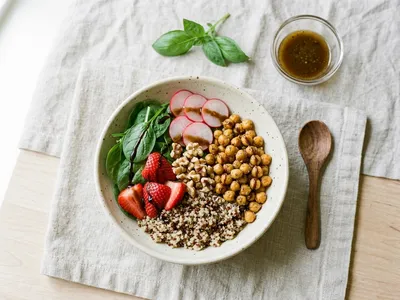 Sommerliche Bowl mit Babyspinat, frischen Erdbeerscheiben, Quinoa, gerösteten Kichererbsen, Radieschen und Walnüssen in einer hellen Schüssel