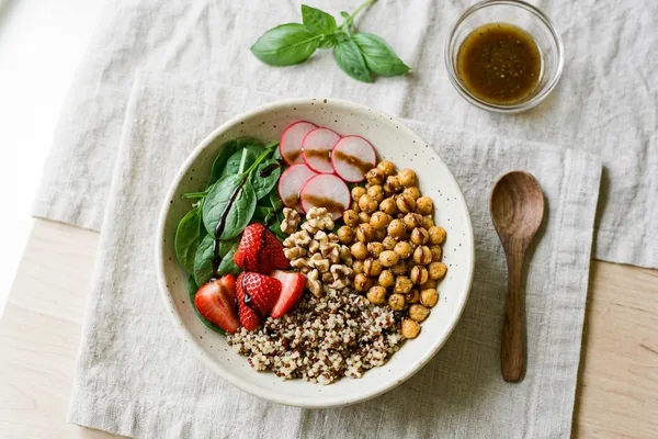 Sommerliche Bowl mit Babyspinat, frischen Erdbeerscheiben, Quinoa, gerösteten Kichererbsen, Radieschen und Walnüssen in einer hellen Schüssel