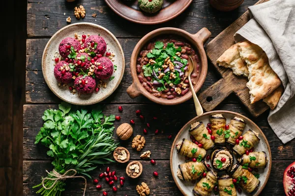 Georgische pflanzliche Tafel von oben: Pkhali aus Roter Bete und Spinat mit Granatapfelkernen, eine Schale Lobio-Bohnen, Auberginenröllchen mit Walnusscreme, frische Kräuter und Fladenbrot auf dunklem Holztisch