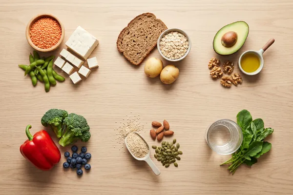 Pflanzliche Lebensmittel nach Nährstoffgruppen sortiert: Hülsenfrüchte, Vollkornprodukte, Nüsse, Samen, Obst und Gemüse auf einem hellen Holztisch