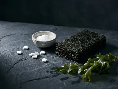 Pflanzliche Jodquellen für vegane Ernährung — Nori-Algenblätter, jodiertes Speisesalz im Schälchen und Jod-Tabletten in moodiger Stillleben-Anordnung