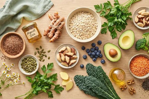 Flatlay pflanzlicher Lebensmittel für gesunde Haut — Leinsamen, Algenöl, Kurkuma, Hafer, Kürbiskerne, Paranüsse, Heidelbeeren, Avocado, Brokkoli, Linsen und Grünkohl